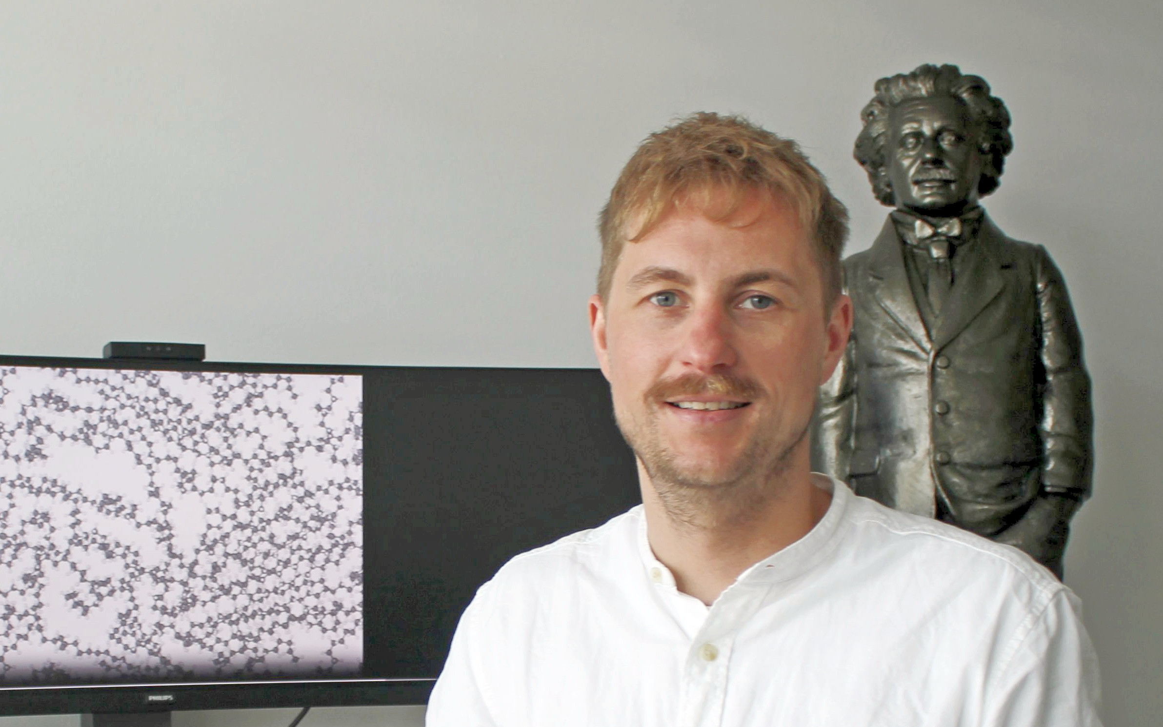 Prof. Dr. Christopher Kuenneth von der Uni Bayreuth trainiert Künstliche Intelligenz mit der chemischen Sprache der Polymere. Der Bildschirm zeigt die Struktur eines Polymers mit C-Atomen (graue Kugeln) und H-Atomen (weiße Kugeln). 